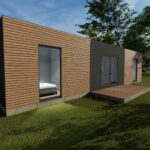 Maison modulaire moderne avec façade en bois et grandes fenêtres en verre, située dans une zone herbeuse avec plusieurs arbres autour, sous un ciel clair et bleu. Une petite terrasse en bois se trouve à l'avant de la maison.