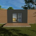 Maison moderne et minimaliste avec un extérieur en bois, de grandes portes doubles en verre, située dans une zone herbeuse avec des arbres en arrière-plan. Intérieur visible avec un canapé jaune et une petite kitchenette.