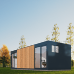 Bureau modulaire moderne avec façade sombre, grandes fenêtres en verre et portes vitrées, panneau en bois sur un côté, situé dans une zone herbeuse avec des arbres bien entretenus et un ciel bleu clair en arrière-plan.