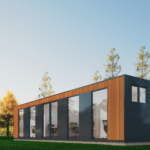 Bâtiment rectangulaire moderne avec grandes fenêtres vitrées, panneaux sombres et lattes en bois, situé dans une zone herbeuse avec des arbres et un ciel clair en arrière-plan.