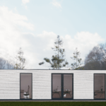 Bureau modulaire moderne avec extérieur blanc, grandes fenêtres et portes en verre avec cadres noirs, chaises de bureau et bureaux visibles à l'intérieur, situé dans un environnement naturel avec des arbres en arrière-plan et un ciel dégagé.