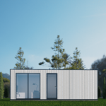 Maison modulaire moderne avec extérieur blanc et élégant, grandes fenêtres en verre, située dans une zone verdoyante avec des arbres élancés et un ciel bleu clair, intérieur visible avec un bureau, une lampe et une chaise.