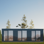 Bureau modulaire moderne avec grandes portes et fenêtres en verre, extérieur sombre, situé dans un environnement naturel avec des arbres et de l'herbe, ciel dégagé avec des montagnes en arrière-plan, meubles de bureau visibles à l'intérieur.