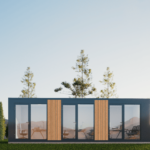 Bureau modulaire moderne avec grandes fenêtres et portes en verre, extérieur en bois vertical, situé dans un environnement naturel avec de l'herbe verte et des arbres élancés, ciel dégagé avec soleil levant ou couchant, meubles visibles à l'intérieur.
