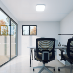 Bureau modulaire moderne avec deux chaises de bureau ergonomiques, bureau blanc avec lampe de bureau, ordinateur portable et livres empilés, grandes portes coulissantes en verre sur le côté gauche, petite fenêtre sur le mur du fond, luminaire carré au plafond.