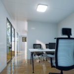 Espace de bureau moderne avec long couloir, grandes fenêtres en verre, sol en bois poli, chaises de bureau, bureaux avec écrans d'ordinateur, environnement de travail propre et bien éclairé.