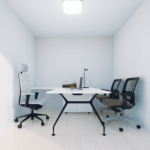 Petit espace de bureau minimaliste avec murs blancs, sol en bois clair, trois chaises de bureau, bureau blanc avec pieds noirs, ordinateur portable, moniteur, lampe de bureau, papiers, bien éclairé par une lumière au plafond.