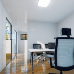 Espace de bureau moderne avec murs blancs, plafond avec luminaire rectangulaire, grandes fenêtres, sol en bois poli, chaise de bureau avec dossier en maille, et bureau avec moniteurs d'ordinateur et fournitures de bureau.