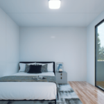 Chambre moderne avec lit, literie blanche, coussins sombres, table de chevet avec lampe et cadre photo, grande fenêtre avec vue sur les arbres, sol en bois, et murs blancs.